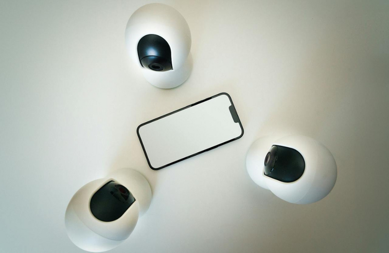 Three webcam type cameras in a triangle, all facing a phone with a blank white screen in the centre. 