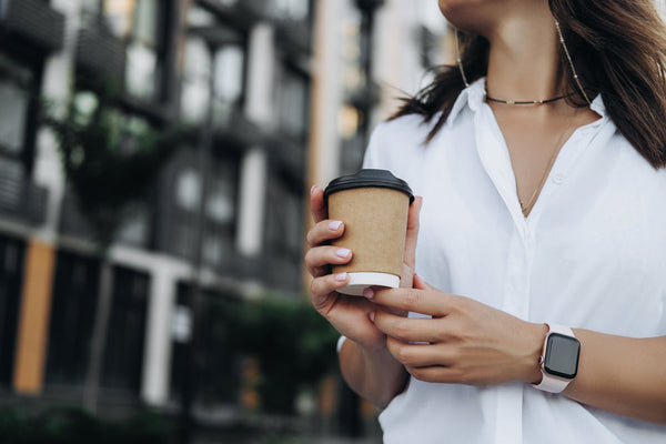 A woman holding a takeaway coffee and wearing an older series Apple Watch