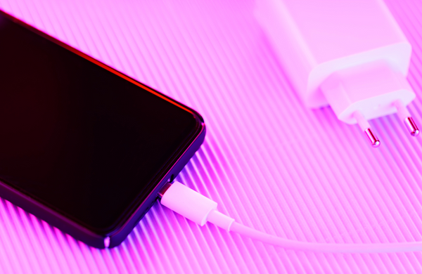 A phone plugged in charging on a bright pink background. 