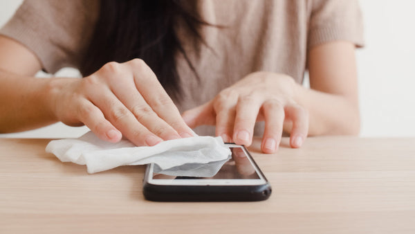 A woman using an alcohol wipe to clean her phone screen.