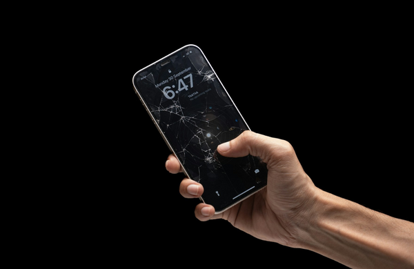 A hand holding an iPhone out with a cracked screen. 