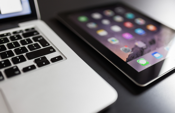 a close up of a MacBook keyboard with an out of focus iPad next to it.