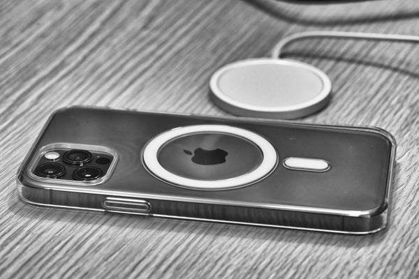 A black and white image of a MagSafe compatible iPhone next to a MagSafe charger. 