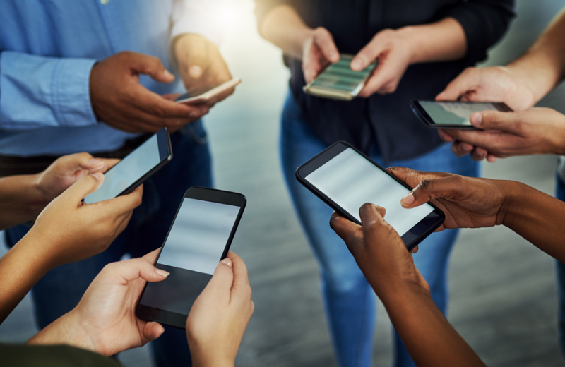 A group of six people standing in a circle all holding their smartphones in both hands.