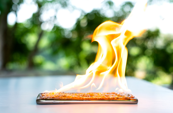 A phone on an outside table with flames coming out of the screen. 