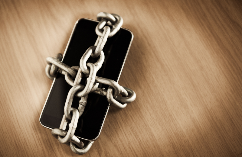 A phone wrapped in thick chains on a wooden surface.