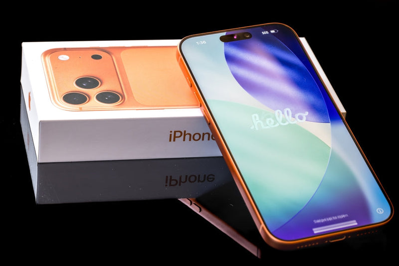 An orange iPhone 17 resting on its manufacturers box displaying the welcome message of 'hello'