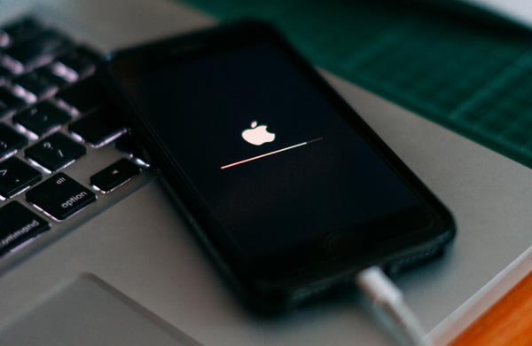 An iPhone resting on the corner of a MacBook. The iPhone is plugged and performing a software update. 