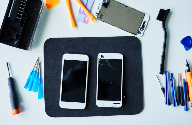 A broken phone and an unblemished phone next to each other surrounded by refurbishing tools.