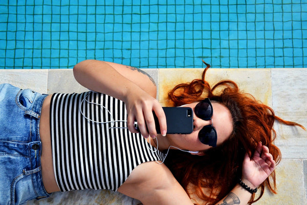 Red haired woman laying next to a swimming pool with a phone in hand