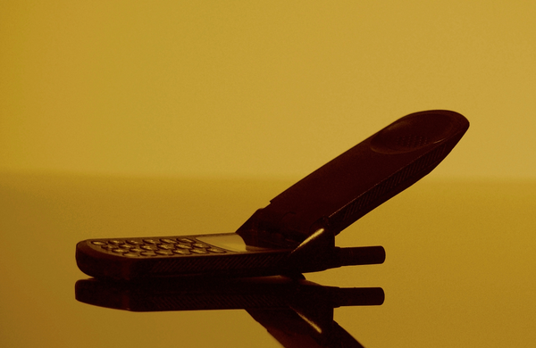 An old school flip phone silhouetted in yellow lighting.