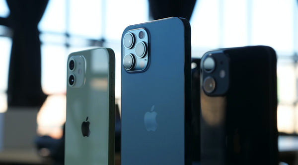 Three different coloured iPhones on display with an out of focus shop in the background