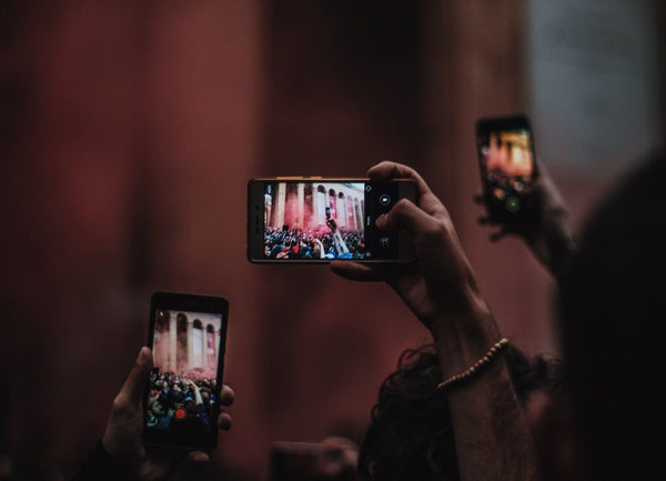 Three phones held in hands above people heads capturing videos at a concert.