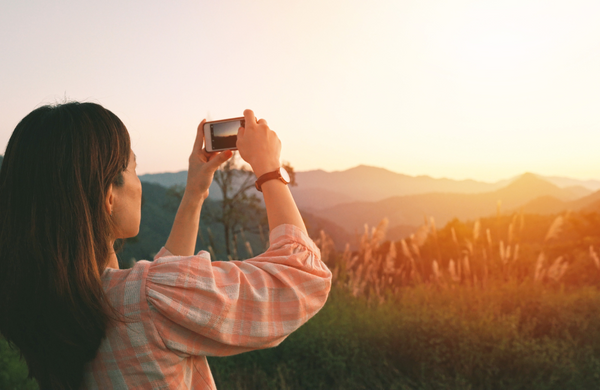 A woman taking a picture of the sunset. 