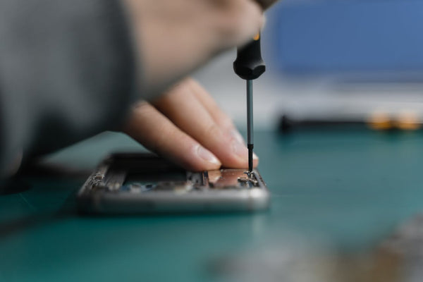 A person holding a screwdriver to a smartphone, refurbishing it.