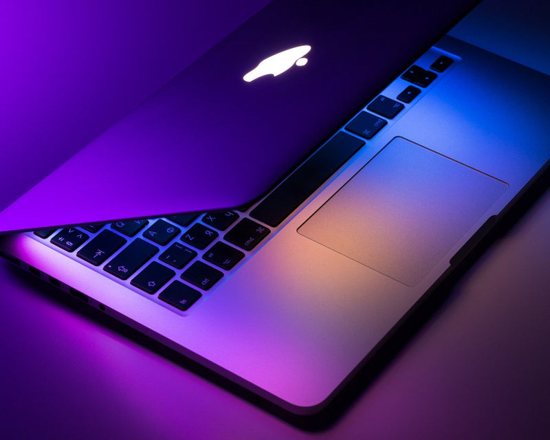 A half open MacBook with a purple, blue and yellow glow